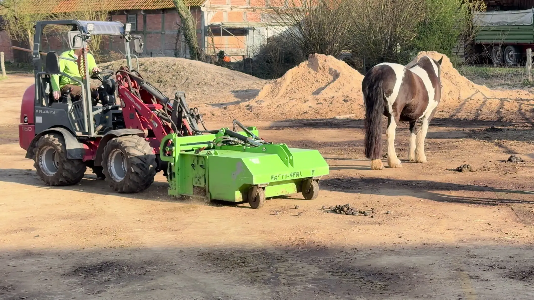 Johann Krahfuß fährt mit dem Weidemann-Hoflader und FARM-SERVANT ECO über den Paddock; dahinter steht ein Pferd
