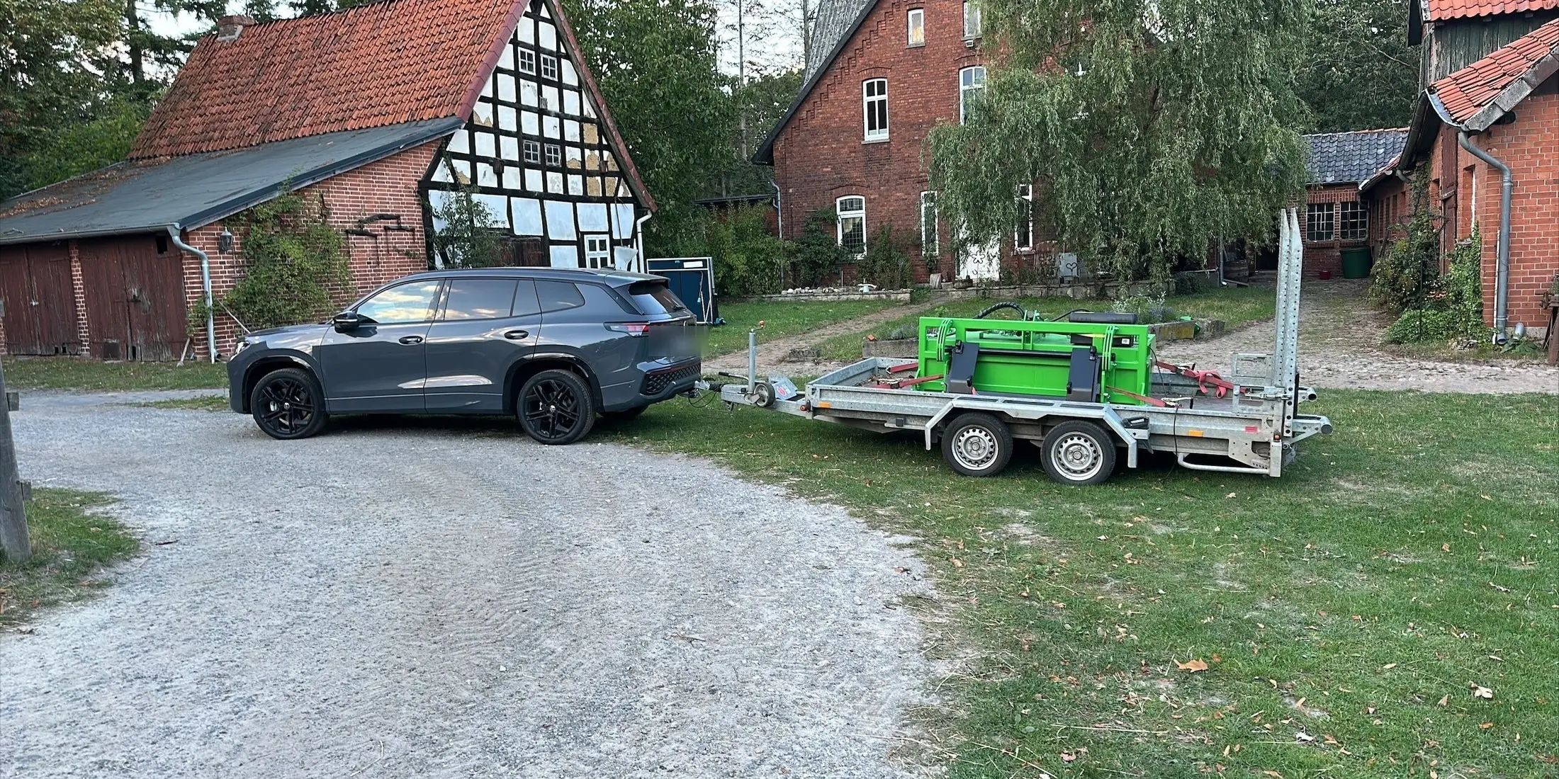 Zugfahrzeug und Anhänger mit einem grünen FARM-SERVANT ECO auf dem Hofplatz vor Fachwerkgebäuden
