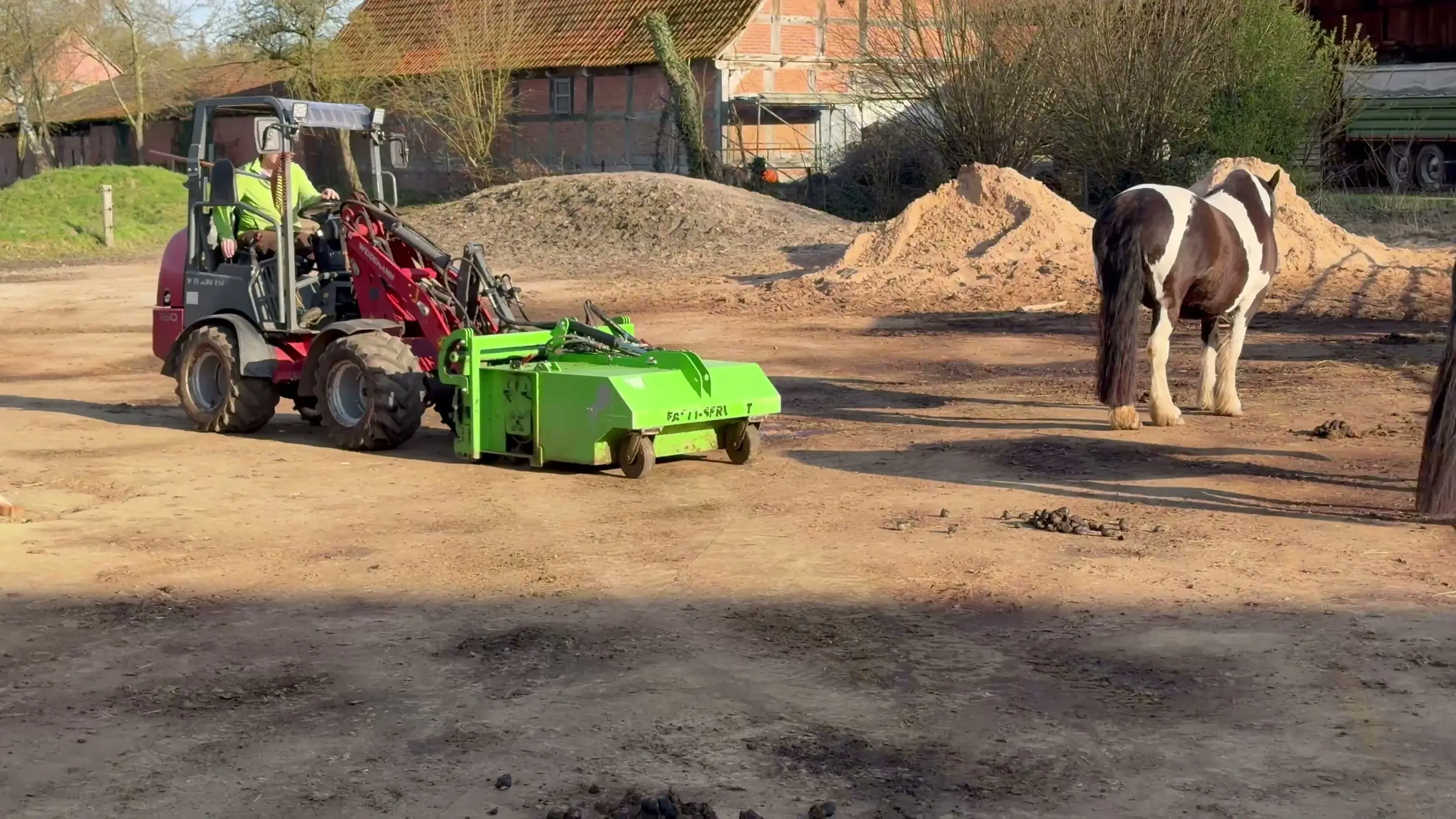 Johann Krahfuß fährt mit dem Hoflader und FARM-SERVANT ECO über den Paddock, rechts zwei Pferde