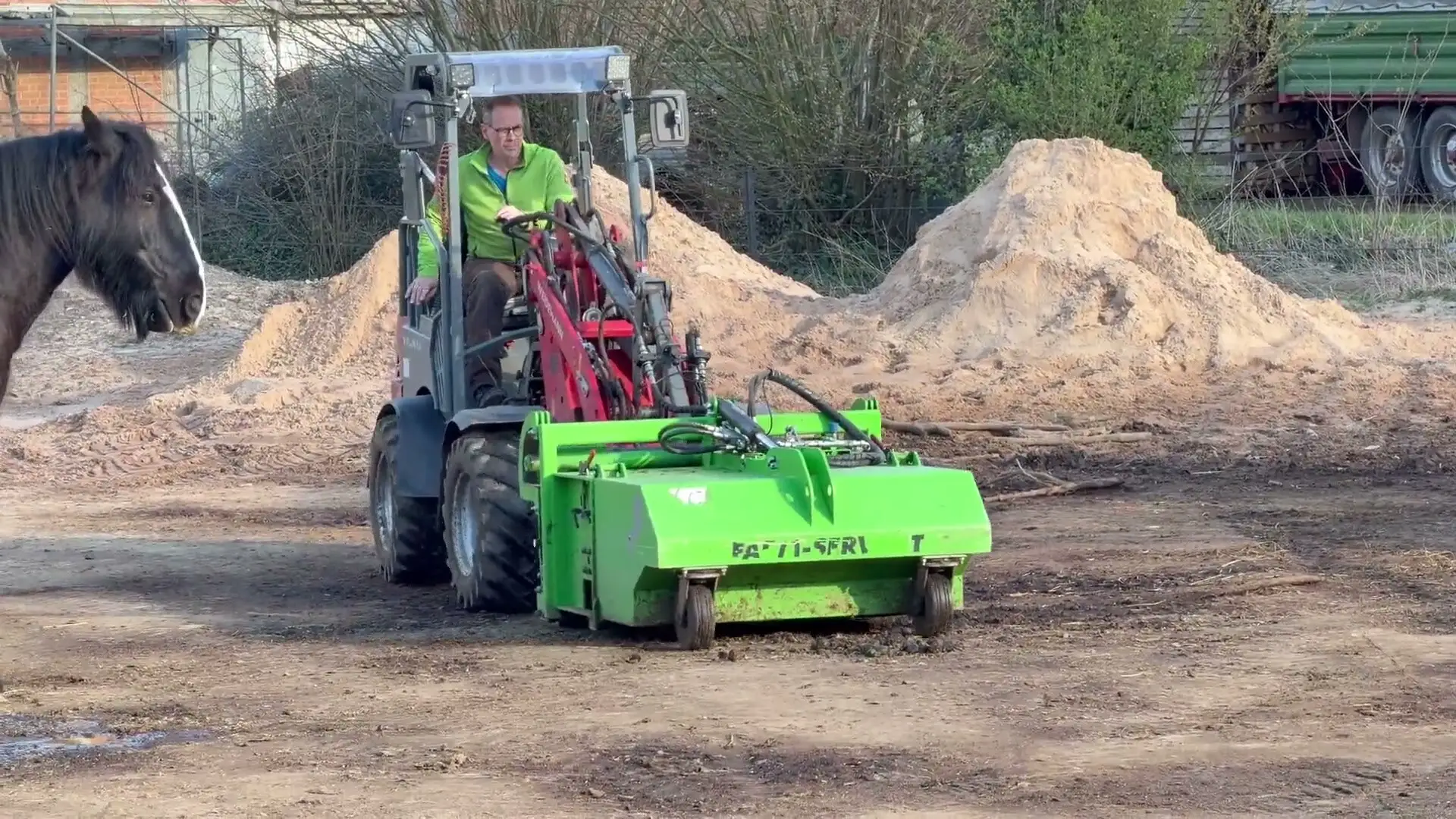 Standbild aus dem Praxisfilm: Hoflader mit Abmistgerät auf dem Paddock